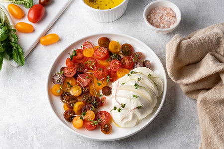Ball of mozzarella cheese with sliced cherry tomatoes on a white plate with vegetables, caprese salad.の写真素材