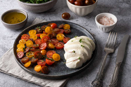 Gray plate with caprese salad, mozzarella cheese with sliced colorful tomatoes, seasoned with olive oilの写真素材