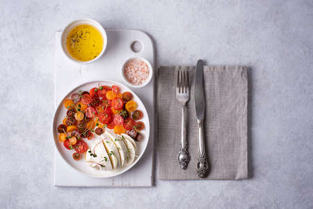 Mozzarella ball on a plate with chopped cherry tomatoes and microgreens with olive oil, caprese salad.の写真素材