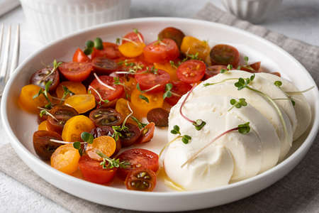 Close-up of mozzarella ball cheese with sliced cherry tomatoes, seasoned with olive oil, white plate with caprese salad.の写真素材