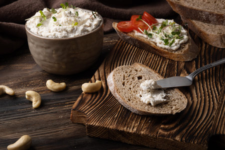 Healthy cream cheese made from fermented nuts, vegan cashew cheese and a slice of bread on a gray...
