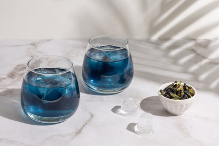Two glasses of anchan from butterfly pea flower on marble background in sunlight, iced healthy...