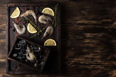 Fresh prawn, frozen shrimps on a tray with lemon and ice cubes on a dark wooden background.の写真素材