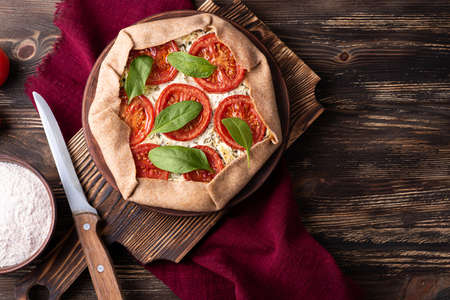 Vegetarian pizza galette with feta cheese and spinach, open pie or tart with tomatoes on wooden background.の写真素材