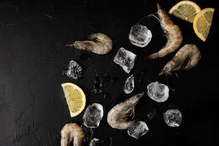 Raw shrimps, prawn with ice cubes and lemon on black background, frozen seafood.の写真素材