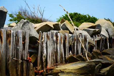 An old wooden fence holding back some large rocks on the beachの写真素材