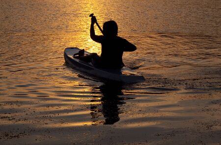 silhouette of a young boy sea kayaking at sunsetの写真素材