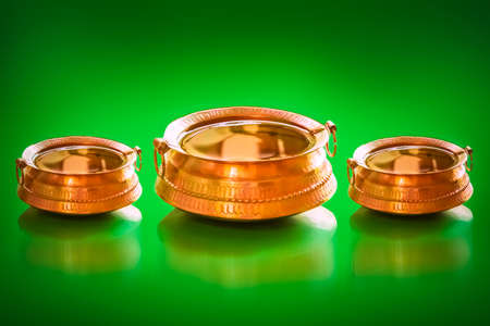 Traditional Brass Pot with full of water and coins inside for lucky charm decorative handles and legs isolated on a green background.の写真素材