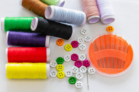 A variety of colorful and white Buttons, Spools of thread in various colors and Sewing needles, on a white background.の写真素材
