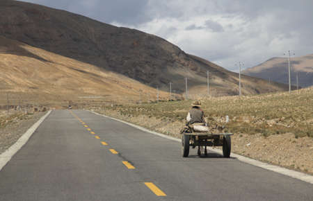 Tibetan farmer ride the horse car on the road running through mountains in Tibet, Chinaの写真素材