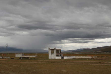 Tibetan house with the dirt road in a cloudy day, Tibet, Chinaのeditorial素材