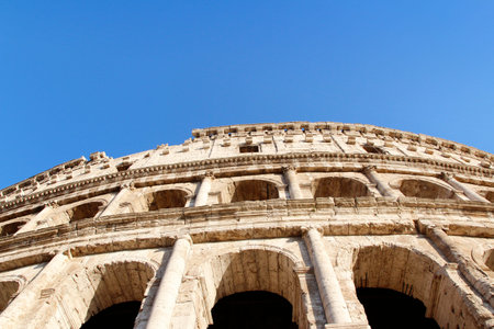 The exterior facade of the Colosseum or Coliseum with the arches against blue clear sky in Rome,...