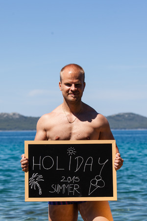 Man holding blacboard with holiday text on beachの写真素材