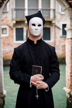 young priest in venice wearing mask  in front of canalの写真素材