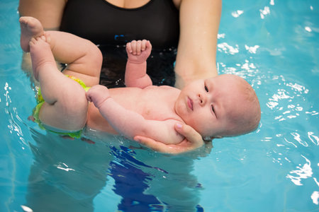 Happy infant baby girl enjoying her first swim in pool