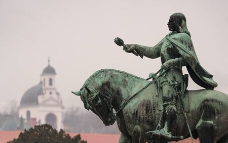 statue of Janos Hunyadi on Szechenyi Square in Pecs, Hungary with chapel at backgroundのeditorial素材