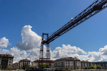 View of the Portugalete suspension bridge structure with the village in the background and clear blue sky with white clouds. In Vizcaya. Basque Countryの写真素材