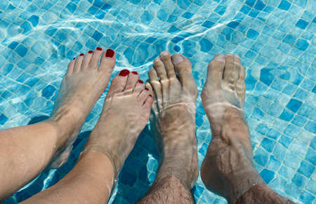 Feet of a couple of men and women, she with her nails painted red in the water of a swimming pool.の写真素材