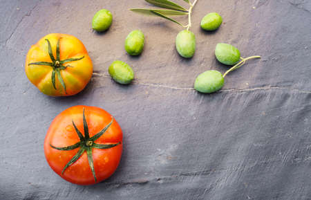 Still life with two organically grown tomatoes and olives, symbols of the Mediterranean diet, on a dark background with copy space to the right of the image.の写真素材