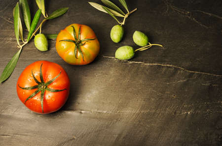 Still life with two organically grown tomatoes and olives, symbols of the Mediterranean diet, on a dark background with copy space to the right of the image.の写真素材