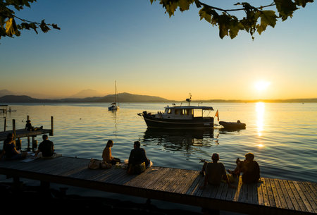 Tranquil sunset scene on Lake Zugersee in the Swiss town of Zug with a pleasure boat, a small wooden...