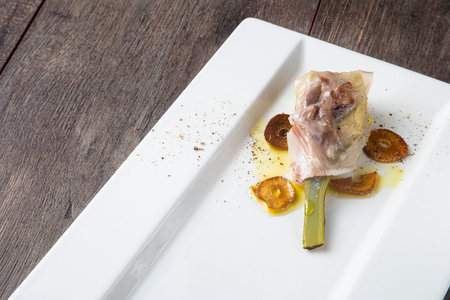 Food still life with artichoke and baked pork jowl with garlic slices on a white plate with wooden board background, with copy space.の写真素材