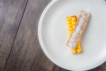 Puff pastry pantxineta with lemon cream and icing sugar on a white plate on a rustic wooden background. Typical dessert from the Spanish Basque Country.の写真素材