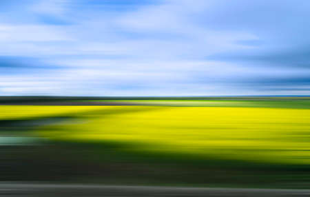 Blurred and shaken image of a landscape in shades of green, yellow and blue to be used as a template or background.の写真素材