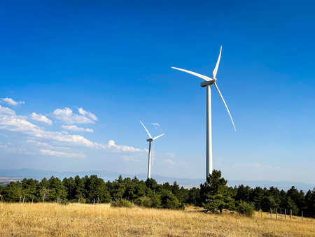 Modern windmills installed on hills in the countryside amidst vegetation.