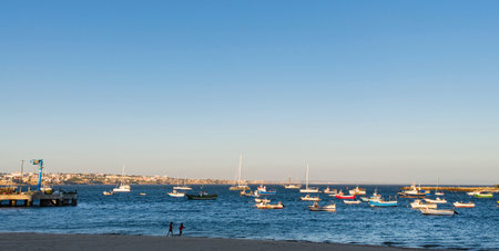 Scenic view of Cascais beach in Portugal during golden hour, with numerous colorful fishing boats and sailboats anchored in the calm Atlantic waters.の写真素材