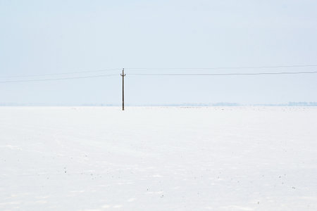 A Lone Electric Pole in Empty Winter Landscape with Snowの写真素材