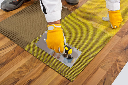 applies tile adhesive on wooden floor with reinforce fiber mesh