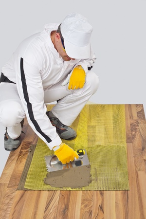 Worker applies tile adhesive with reinforcement mesh on wooden floorの写真素材