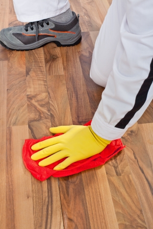 Worker cleans with red duster old wooden floor before tilling and removes dirt, dust and greasy spotの写真素材