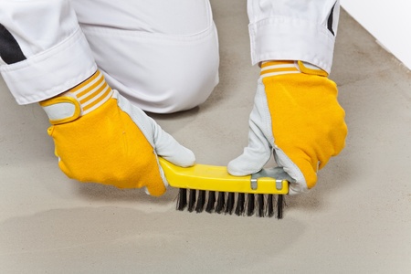 hands with yellow gloves with wire brush cleans the cement substrate floor before tillingの写真素材