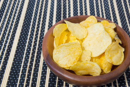 Potato chips in wooden bowl on bamboo Mat background.
