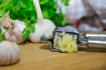 Crushing garlic to add to the dish. Whole and chopped garlic on a cutting board made of natural oak. Fresh parsleyの写真素材