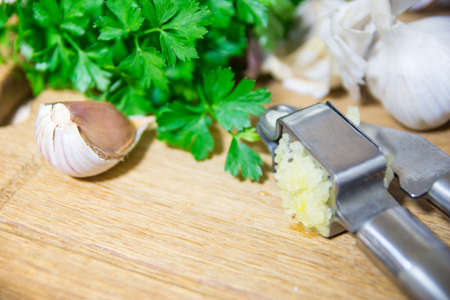 Crushing garlic to add to the dish. Whole and chopped garlic on a cutting board made of natural oak. Fresh parsleyの写真素材