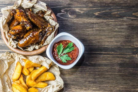 Chicken wings in a fragrant and pungent sauce with sesame seeds. A glass of fresh cold beer and fried potatoes with rustic tomato sauce from fresh tomatoes and herbsの写真素材
