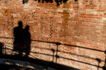 In an old wall in the Italian city of Venice can see the shadows of tourists walking in the sunsetの写真素材