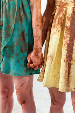 Close-up of two unrecognizable women in bright dresses dirtied in chocolate holding hand in handの写真素材