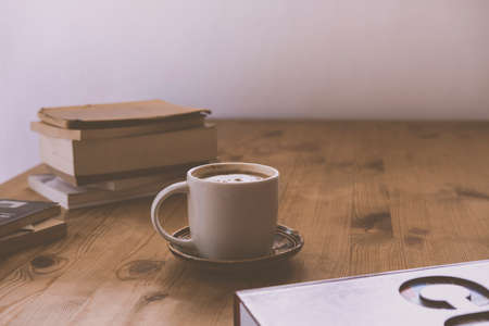 white cup with cappuccino coffee and a small tower of books on a rustic wooden tableの写真素材