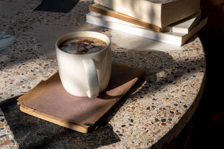 white cup with cappuccino coffee and books on an old table with a background of old rustic woodsの写真素材