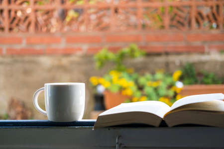 white cup with cappuccino coffee in a window overlooking a flowered terraceの写真素材