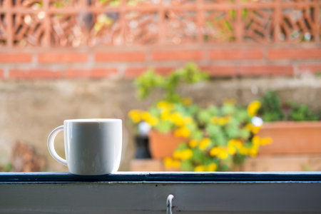 white cup with cappuccino coffee in a window overlooking a flowered terrace