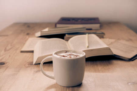 white cup with cappuccino coffee accompanied by a series of books on a rustic wooden tableの写真素材