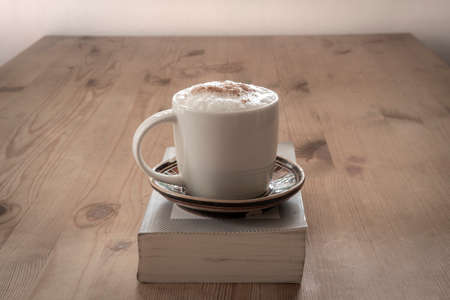cup with coffee and a closed book on a rustic wooden tableの写真素材