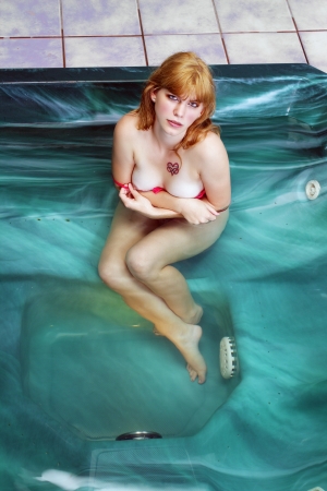 A lovely, young, topless blonde sits in her spa, wearing sexy lingerie.  Isolated on a white background with generous copyspace.の写真素材