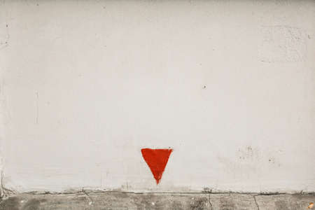 White rough concrete wall with with red arrow turned top down. White wall and painted red triangleの写真素材