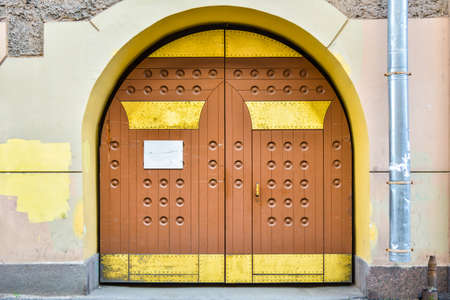 A closed grunge brown wood old door with decorative embossed round elements and gold metal plates with nails. A wood gate inside stone archの写真素材